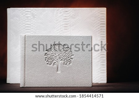 Composition of photo books in natural white leather of different sizes. The white paper on a dark background.