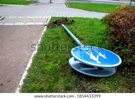 uprooted blue road sign at the pedestrian zone and cycle path. pedestrian and bicycle symbol. lies upright even with a concrete foundation on the ground by the sidewalk on the grass.