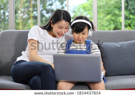 Asian mother teaching her daughter to learn from online class using laptop for homeschooling and education concept