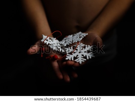 
Children's hands hold wooden Christmas tree decorations in the form of snowflakes. Dark background. Image with a selective focus