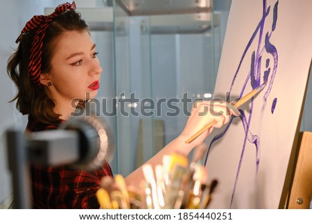 young pretty woman artist with brush near easel draws picture