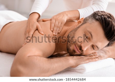 Closeup of handsome man having full body massage at male spa. Unrecognizable female therapist rubbing middle aged man shoulders, making relaxing massage. Spa, massage, cosmetology for men Royalty-Free Stock Photo #1854442684
