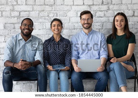 People and gadgets diversity. Group portrait of confident happy young friends men and women of caucasian indian african ethnicities sitting in row looking at camera holding phones computers in hands