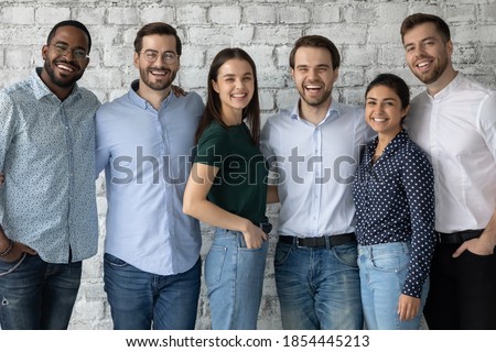 When colleagues are friends. Group portrait of happy positive diverse young people of different gender and race coworkers teammates standing by brick wall close together hugging and looking at camera