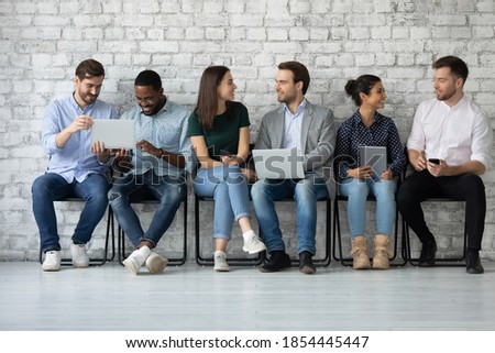 Sharing information. Diverse young people of millennial generation sitting in line talking chatting communicating using electronic devices sharing data discussing apps software new models of gadgets Royalty-Free Stock Photo #1854445447