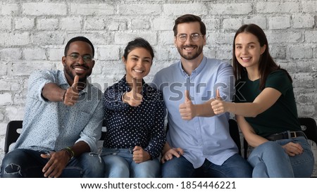 Lucky ones. Portrait of four happy satisfied multiethnic persons sitting on row of chairs in office looking at camera showing thumbs up being hired recruited getting good positions in corporate staff Royalty-Free Stock Photo #1854446221