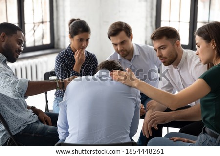 On group therapy session. Compassionate diverse multiethnic men and women gently touching shoulders of crying suffering male teammate sharing his personal problem expressing support care understanding Royalty-Free Stock Photo #1854448261