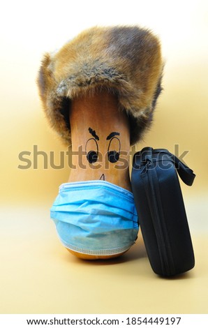 pumpkin in mask because of covid with ushanka hat and suitcase on neutral orange background