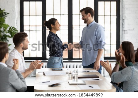 Young caucasian male ceo handshaking with indian female team member on briefing showing respect to her qualification, gratitude for help, recognition of her efforts in developing corporate business Royalty-Free Stock Photo #1854449899