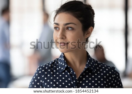 Looking forward. Concentrated ambitious indian businesswoman distracted from work in office smiling and looking aside dreaming about leadership, planning work moments, visualizing successful strategy