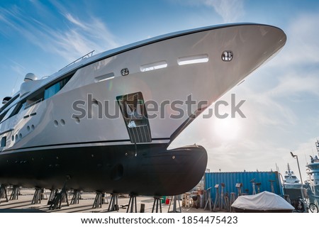 Wide shot of the bow of a new  white modern superyacht on dry dock, with a bulbous bow on a sunny day, with stainless steel  anchor on a sunny day with blue sky Royalty-Free Stock Photo #1854475423