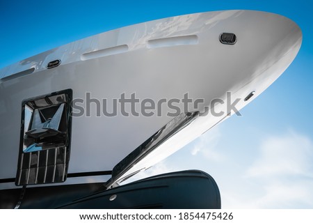 Closeup detail of the bow of a new  white modern superyacht on dry dock, with a bulbous bow on a sunny day. With stainless steel  anchor. Royalty-Free Stock Photo #1854475426