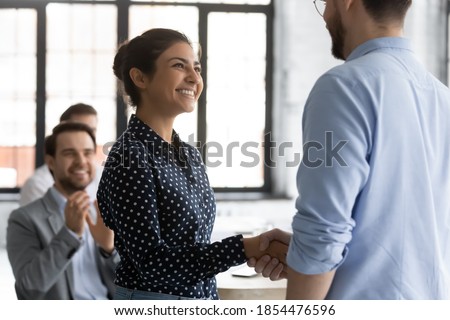 It is an honor to me. Glad smiling young lady corporate worker of indian ethnicity getting recognition acknowledgement of ceo, handshaking higher executive on briefing conference, being hired promoted Royalty-Free Stock Photo #1854476596