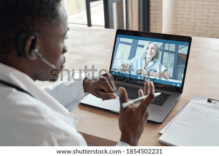 Black male doctor consulting senior old patient by telemedicine online video call. African physician using telehealth medical chat virtual healthcare appointment on laptop computer. Over shoulder view Royalty-Free Stock Photo #1854502231