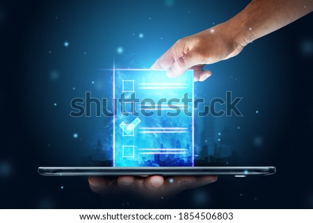 Online voting, Hand with a hologram ballot and a box for Internet voting in a mobile phone on a blue background. Mixed environment, e-voting technology concept Royalty-Free Stock Photo #1854506803