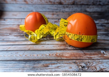 Overhead view of persimmon fruit on wooden table with tape measure.