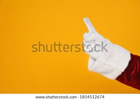 Santa Claus pointing at something on yellow background, closeup of hand. Space for text