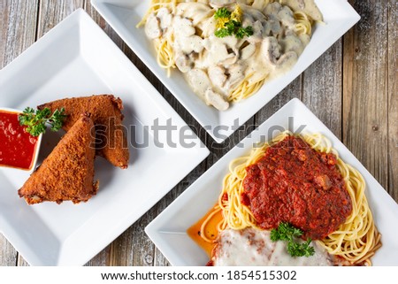 A top down view of several Italian entrees on a wooden table surface, featuring deep fried mozzarella, and spaghetti.