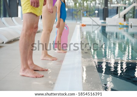 Legs of contemporary family of father, mother and their little daughter standing by poolside at leisure center and going to dive into water