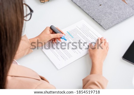 Young brunette businesswoman underlining main points and terms of contract with blue highlighter while reading the text by workplace Royalty-Free Stock Photo #1854519718