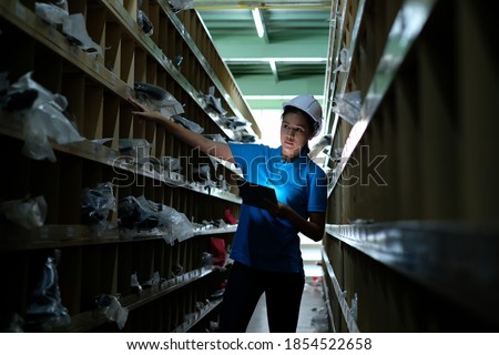 Industrial engineer woman wearing helmet and holding tablet  inspecting spare parts stored on the shelf of factory.Auto parts warehouse for distribute product to customers. Royalty-Free Stock Photo #1854522658