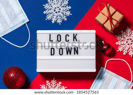 Text Lockdown on the lightbox on two tone red and blue background with decorative snowflakes and craft gift boxes. Christmas holidays in lockdown and quarantine time concept.