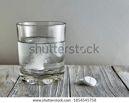 Effervescent tablet in a glass, next to two more tablets on a wooden table
