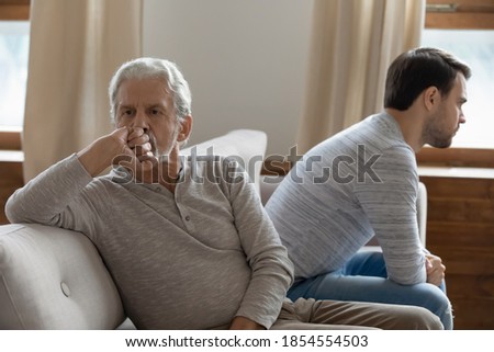 Unhappy mature father and adult son not taking after quarrel, sitting on couch at home separately back to back, upset older grandfather and grandson ignoring each other, two generations conflict Royalty-Free Stock Photo #1854554503