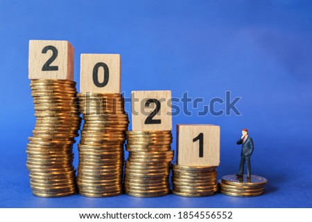 2021 Business and planning Concept. Businessman miniature figure people standing on  stack of coins with wooden number block toy on blue background