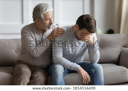 Caring loving mature father calming hugging upset adult son, sitting on couch, senior older grandfather comforting supporting unhappy grandchild, helping to overcome problems, two generations Royalty-Free Stock Photo #1854556690