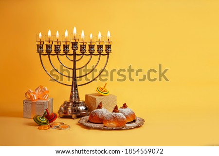 Image of Jewish holiday Hanukkah with menorah (traditional Candelabra), donuts and wooden dreidels (spinning top), doughnut, chocolate coins on a yellow background. Royalty-Free Stock Photo #1854559072