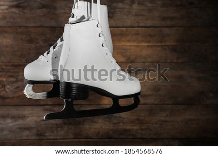 Pair of white ice skates hanging on wooden background. Space for text
