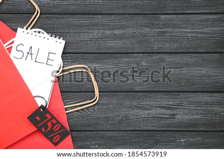 Inscription Sale with paper shopping bags and sale tag on black wooden background