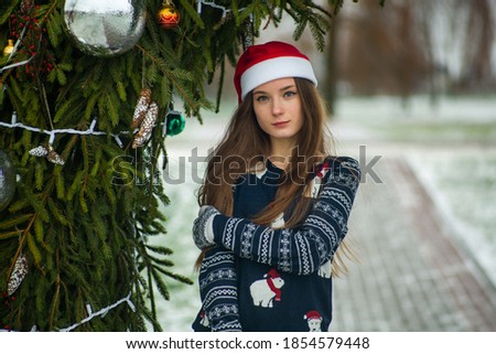 Young pretty white caucasian teen girl with long hair and in a hat of Santa Claus outdoors. Lifestyle.