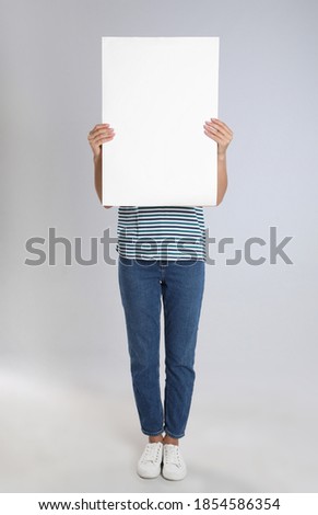 Woman holding blank poster on light grey background