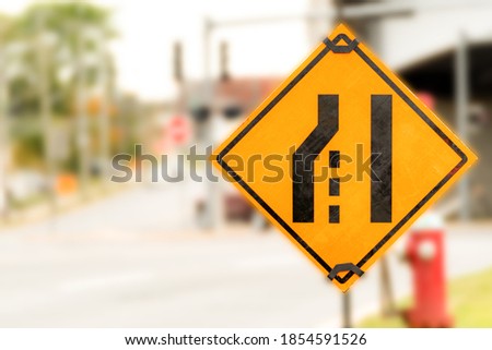 A black on yellow Left Lane Ending road sign. No words, pictograph only. Shallow depth of field. Room for text.
