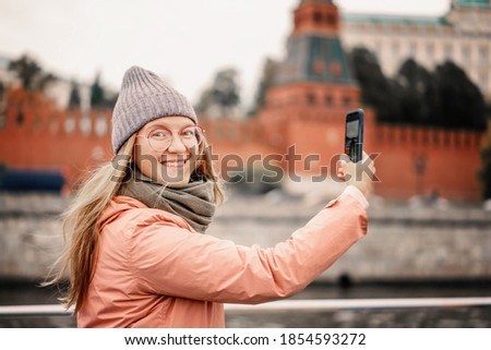 Red-haired woman in glasses traveler in a hat and jacket chatting on a smartphone taking a selfie Moscow