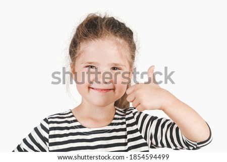 Close up portrait of happy girl looking at camera and showing thumb up. Posing little girl wearing striped shirt. Girl showing support, respect to someone. Isolated background. I like that. Good job.