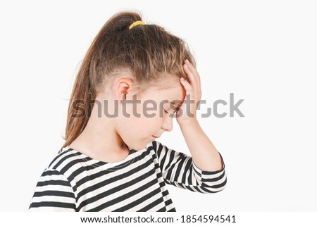 Facepalm. Upset girl with closed eyes and hand holding on her forehead. Frustrated forgetful girl with head tilted forward down. Posing a little girl wearing a striped shirt. Isolated white background