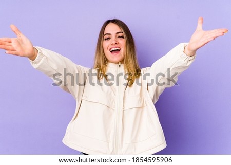 Young caucasian woman isolated on purple background feels confident giving a hug to the camera.