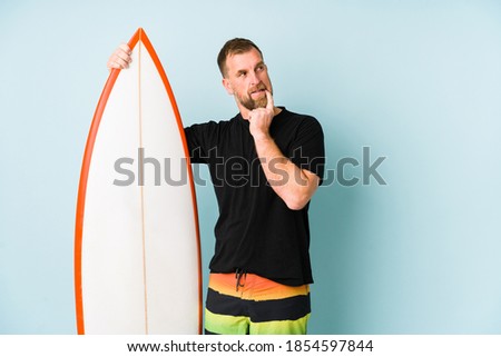 Surfen man isolated on blue background relaxed thinking about something looking at a copy space.