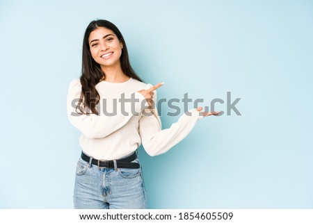 Young indian woman isolated on blue background excited holding a copy space on palm.