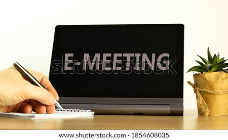 E-business concept. Tablet with text 'e-meeting'. Online business and education during COVID-19 quarantine. Male hand with pen, house plant. Copy space.
