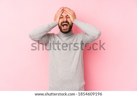 Young long hair man isolated on a pink background laughs joyfully keeping hands on head. Happiness concept.