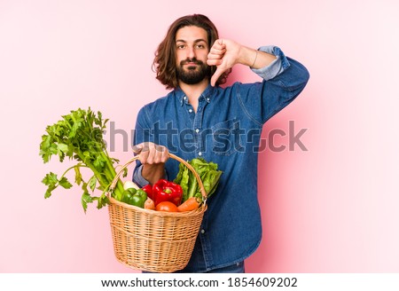 Young man picking organic vegetables from his garden isolated showing a dislike gesture, thumbs down. Disagreement concept.