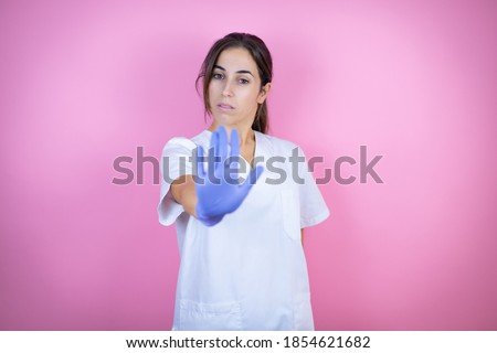 Young doctor girl wearing nurse or surgeon uniform with latex gloves over isolated pink background