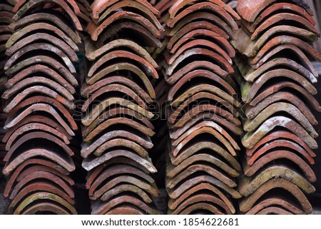 Curved edges of neatly stacked pile of old terracotta roof tiles covered in lichen and signs of ageing, ready for recycling or reuse in construction