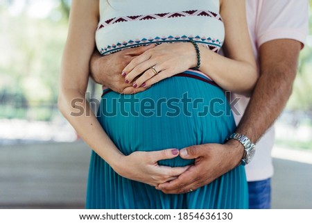 Close up of the belly of pregnant girl in blue dress with her hands of her husband