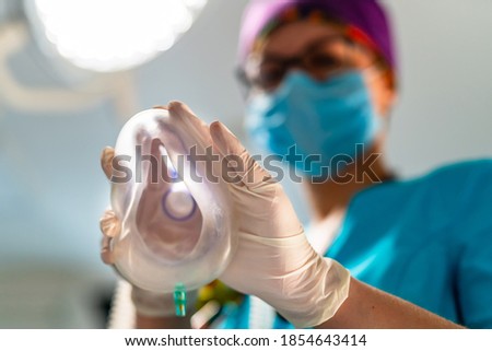 Oxygen mask from the eyes of a patient. Female anesthesiologist in scrubs putting anesthetic mask on a camera. Royalty-Free Stock Photo #1854643414