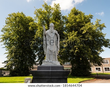 White statue of a bishop with big trees in the background. Bishop William Kinsella's statue, in Kilkenny, Ireland